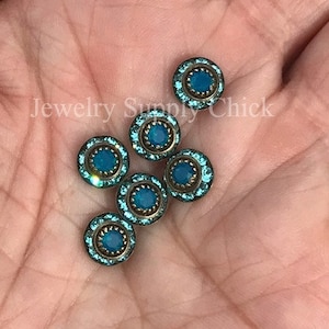 May include: A close-up of six turquoise blue rhinestone embellishments with a gold metal setting. The rhinestones have a faceted design and are arranged in a cluster.