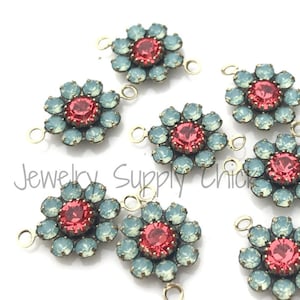 May include: Several flower-shaped jewelry components. Each component features a central red crystal surrounded by light blue crystals. The components have gold-colored loops for attachment and are set against a white background. The text "Jewelry Supply Chick" is visible.