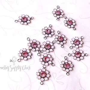 May include: A collection of floral-shaped jewelry connectors. Each connector features a central pink gemstone surrounded by white opalescent stones. The connectors are connected by small loops and are set against a white background.