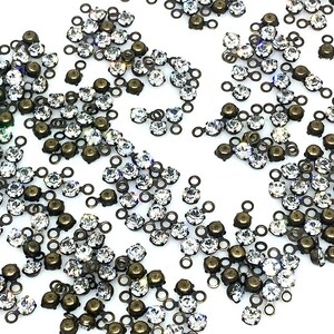 May include: A scattering of antique bronze-toned metal settings with clear crystal rhinestones. Each setting has two loops for attaching to a jewelry piece.