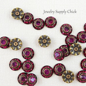 May include: Assortment of 18 small, round, antique gold-toned metal embellishments with a raised, scalloped edge. Each embellishment features a central, round, fuchsia-colored rhinestone surrounded by smaller rhinestones.