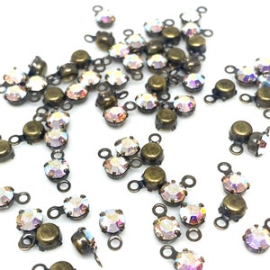May include: A group of antique brass settings with clear iridescent rhinestones. Each setting has two loops for attaching to a project.