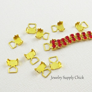 May include: A close-up of a red rhinestone chain with gold metal clasps. The chain is made of small, square rhinestones that are set in a gold metal frame. There are several extra clasps scattered around the chain.
