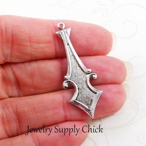 以下が含まれることがあります： 銀色のジュエリーペンダント。装飾的で細長いデザイン。ペンダントはテクスチャ加工された表面と、チェーンなどに取り付けるための上部の小さなループが特徴です。ペンダントの下部はひし形です。