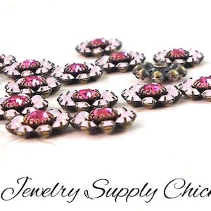 May include: Close-up of several flower-shaped jewelry components. Each component features a central pink gemstone surrounded by clear, petal-shaped stones. The metal setting has a bronze finish. The text "Jewelry Supply Chick" is at the bottom.