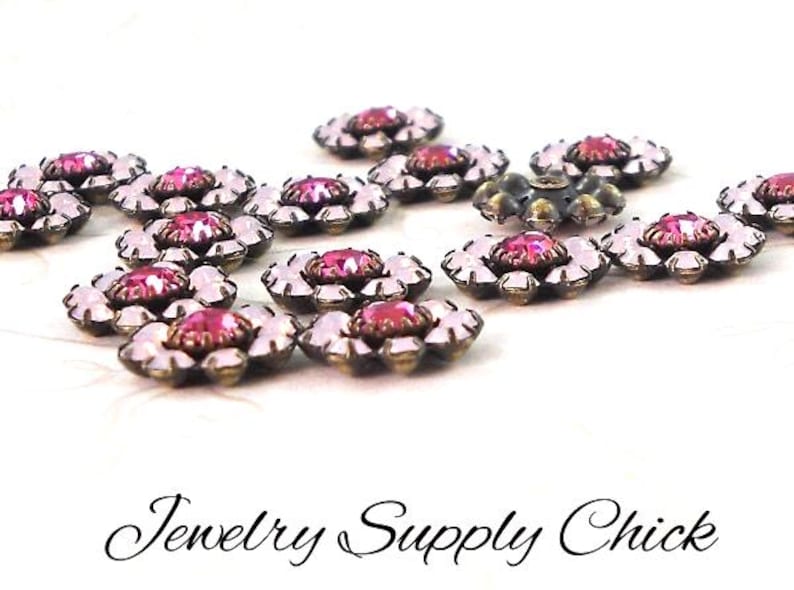 May include: Close-up of several flower-shaped jewelry components. Each component features a central pink gemstone surrounded by clear, petal-shaped stones. The metal setting has a bronze finish. The text "Jewelry Supply Chick" is at the bottom.