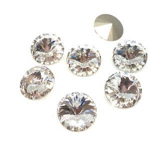 May include: A group of seven clear glass rhinestones with a faceted design. The rhinestones are round and have a flat back.
