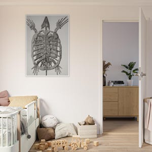 May include: A framed grayscale print of a turtle skeleton. The artwork is displayed on a white wall in a room with a child's bed, pillows, and wooden toys. The print has a white border.