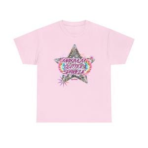 Puede incluir: Camiseta rosa claro con un diseño de estrella brillante y la frase "MAXIMUM GLITTER SPARKLE" en letras coloridas. La estrella tiene un borde de arcoíris.