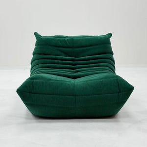 May include: A green corduroy lounge chair with a low profile and a unique, modern design. The chair features a series of horizontal, pleated sections, creating a textured appearance. The chair is a deep, forest green color.