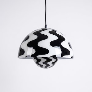 May include: A modern pendant light with a black and white wavy pattern. The light fixture has a rounded, dome-shaped shade and a smaller, spherical element below, both with the same design. The light hangs from a black cord.