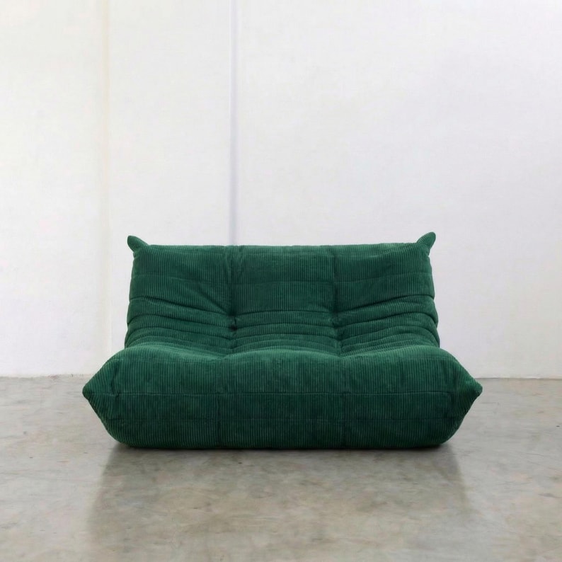 May include: A green corduroy lounge chair with a low profile and rounded edges. The chair has a tufted design and a soft, inviting appearance. The color is a deep, rich green, suitable for a living room or den.
