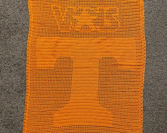 May include: Orange crocheted blanket with a geometric pattern. The blanket is made with a fine yarn and has a delicate texture.
