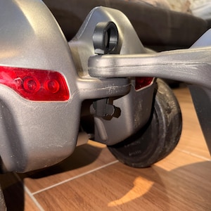 Könnte beinhalten: Nahaufnahme einer grauen, rollenden Fahrzeugkomponente aus Kunststoff. Die Komponente hat ein rotes Rücklicht und einen schwarzen, kreisförmigen Aufsatz. Das Rad ist schwarz und das Fahrzeug steht auf einem Holzboden.