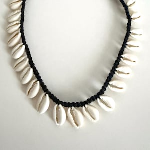May include: A black cord necklace adorned with white seashells. The shells are evenly spaced along the necklace, creating a natural, beachy aesthetic. The necklace has an adjustable length.