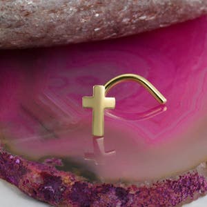 May include: Gold nose ring with a cross charm. The ring is curved and the cross is flat.