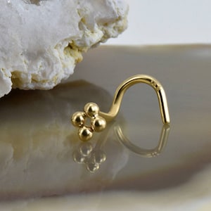 Puede incluir: Un aro de nariz de oro con un pequeño diseño de flor. La flor está hecha de cinco pequeñas cuentas redondas.