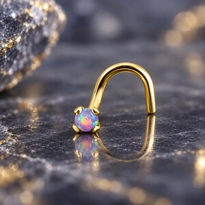 May include: A gold-toned nose stud featuring a curved post and a prong-set, round, iridescent opal stone that displays flashes of pink, blue, and orange. The jewelry piece is designed with a smooth, polished finish and a secure four-prong setting.