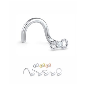 Puede incluir: Un aro de nariz plateado con un cristal transparente en el centro de un diseño de doble bucle. El aro es curvo y tiene un pequeño gancho en el extremo. La imagen también muestra el aro en oro, oro rosa y plata.