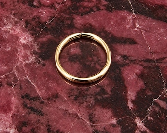 May include: A polished gold-tone circular hoop ring featuring a seamless, continuous band design with a smooth, reflective surface. The ring is a simple, circular shape with a small, barely visible opening where the two ends meet, creating a clean look.