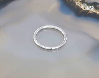 Puede incluir: Un anillo de piercing corporal plateado sin costuras. El anillo está hecho de acero quirúrgico y es una opción popular para piercings en la nariz, los labios o las orejas.