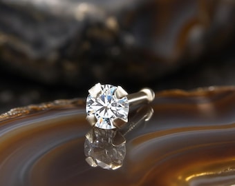 May include: A nose stud featuring a round, brilliant-cut clear gemstone held in a four-prong silver-toned metal setting. The jewelry piece has a straight post with a small rounded end, reflecting light clearly on its faceted surface.