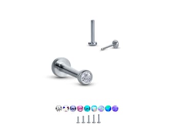 May include: A silver nose stud with a clear round gemstone. The stud is shown with a variety of colored gemstones, including clear, blue, purple, pink, turquoise, and opal.