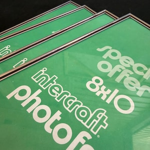 May include: A set of four rectangular photo frames with thin metallic silver borders. Each frame contains a green insert with white text that reads "special offer 8x10" and "intercraft photo". The frames are stacked slightly offset from each other.
