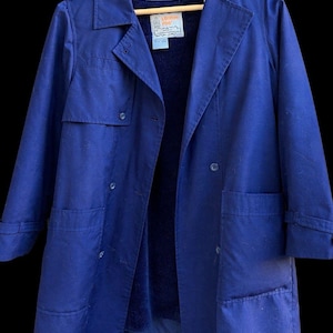 May include: A vintage blue trench coat with a collared neckline, double-breasted button closure, and large pockets. The coat has a dark blue interior lining and is hanging on a wooden hanger. The label reads "London Fog".
