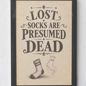 May include: A framed wall art print on aged paper featuring the text LOST SOCKS ARE PRESUMED DEAD in dark gray lettering. Below the text, a single striped sock sits next to a ghostly, translucent sock illustration with two small eye holes.