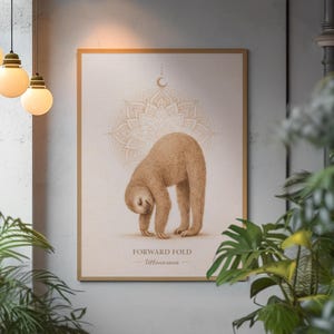May include: A framed print featuring a brown sloth in a yoga pose, labeled "Forward Fold" with the Sanskrit term "Uttanasana." The artwork has a beige background with a mandala design and a crescent moon. The frame is a light brown color.