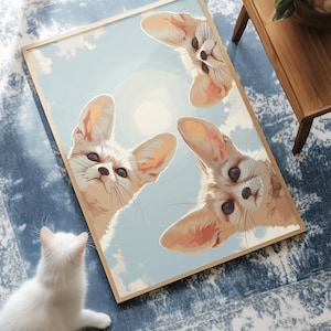 Op de afbeelding: Een ingelijste muurkunstprint met drie woestijnvossen met grote oren die naar beneden kijken vanuit een lichtblauwe lucht met witte wolken en een bleke zon. De vossen hebben een beige vacht, donkere ogen en lange snorharen in kikkerperspectief.