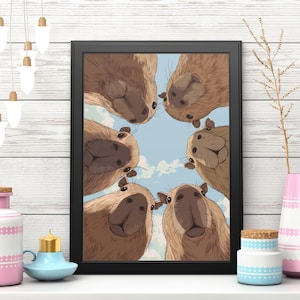 May include: A framed art print featuring a group of capybaras looking down at the viewer. The artwork has a blue sky background with fluffy white clouds. The frame is black. Decorative items include a pink and white vase, a blue candle holder, and a small jar.
