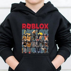 Może przedstawiać: Czarna bluza z kapturem z napisem "ROBLOX" w czerwonych blokowych literach na g&oacute;rze. Poniżej słowo "ROBLOX" jest powt&oacute;rzone pięć razy, a każda litera wypełniona jest innym obrazem. Bluza ma przednią kieszeń.
