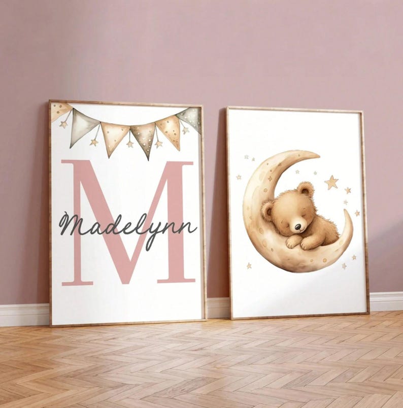 May include: Two framed nursery art prints. One features a pink letter "M" with the name "Madelynn" and a banner of stars. The other shows a sleeping teddy bear on a crescent moon with stars.