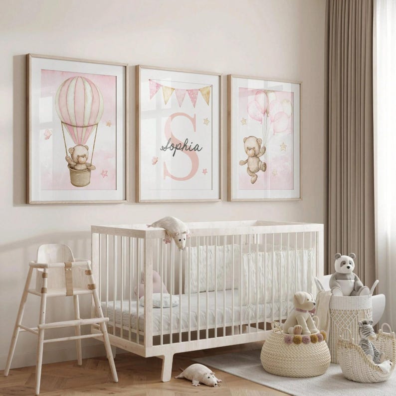 May include: Three framed nursery art prints with a soft pink and beige color scheme. One print features a teddy bear in a hot air balloon, another displays the name "Sophia", and the third shows a teddy bear with balloons. A white crib and high chair are in the foreground.