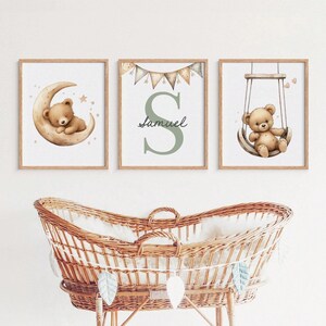 May include: Three framed nursery art prints. One features a teddy bear on a crescent moon, another displays the name "Samuel" with a large letter "S", and the third shows a teddy bear on a swing. The frames are light brown.