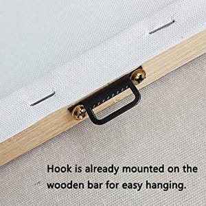 May include: Close-up of a canvas print's wooden frame with a pre-installed black metal hook. The canvas is white, and the frame is light brown. The text reads: "Hook is already mounted on the wooden bar for easy hanging."