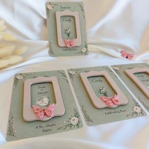 May include: Wedding invitation cards with a light green background, floral accents, and a pink frame. Each card features a pink butterfly and the names "Emily & Daniel". The text "A New Chapter Begins" and "Celebrating Love" are also visible.