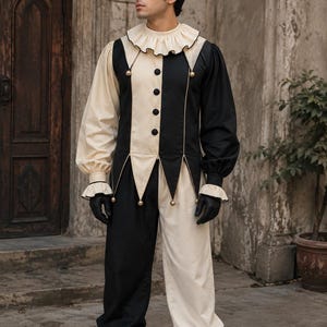 May include: A two-toned black and cream jester costume featuring a long-sleeved tunic with a ruffled collar, four central buttons, and pointed hem details with small gold bells. The matching trousers are colour-blocked in black and cream.