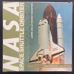 May include: A box depicting the NASA Space Shuttle Orbiter Endeavour (OV-105) with SRB (Solid Rocket Booster). The box has a blue and green background with the shuttle model in white, brown, and black. The text "NASA" and "1/400 Premiere Collection" are visible.