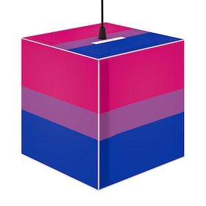 May include: A cube-shaped pendant light fitting featuring a horizontal striped pattern in magenta, purple, and blue. The lamp is suspended by a thin black cord attached to the centre of the top panel, which also displays the same colour scheme.