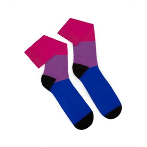 Peut inclure: Une paire de chaussettes montantes avec un motif à blocs de couleurs horizontales. La section supérieure est rose vif, la section centrale est violette et la section inférieure est bleue. Les talons et les pointes sont en tissu noir uni.