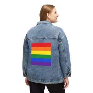 May include: A light-wash denim jacket featuring a rainbow flag design on the back. The flag is a rectangle with horizontal stripes in red, orange, yellow, green, blue, and purple. The jacket has a classic button-up design.