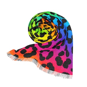 May include: A rolled, colorful scarf with a leopard print design. The scarf features a vibrant gradient of colors, including pink, orange, yellow, green, and blue, with black spots. The edges are finished with a fringe.