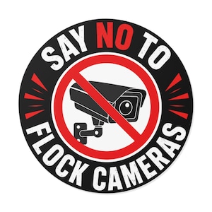 May include: A circular sticker with a black background and a red border. It features a white graphic of a security camera crossed out by a red diagonal line. The text reads SAY NO TO FLOCK CAMERAS in white, with the word NO highlighted in red.