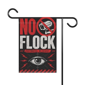 May include: A rectangular garden flag hanging on a black metal stand. The flag features a black background with red and white text reading NO FLOCK and THEY WATCH. WE RESIST. It includes a graphic of a security camera and a large human eye.