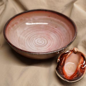 May include: A ceramic bowl and small dish with a reddish-brown rim and a light pink interior. The bowl has a spiral design in the center. The small dish is a shell shape with a reddish-brown and white design.