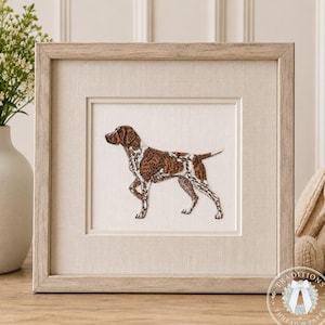 May include: A square, light-toned wooden frame containing a fabric-mounted embroidery of a brown and white spotted dog standing in profile. The dog is depicted with its head turned slightly, showcasing detailed stitching on its coat and legs.