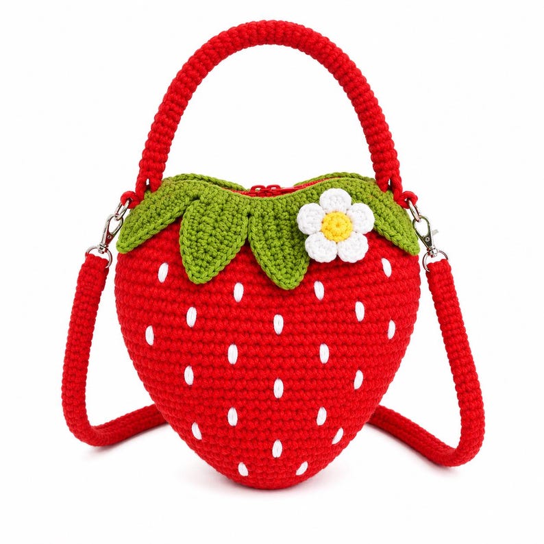 Puede incluir: Un bolso de ganchillo en forma de coraz&oacute;n de color rojo brillante con semillas blancas bordadas. Presenta un borde de hojas verdes de ganchillo en la parte superior, una peque&ntilde;a flor blanca y amarilla, un asa roja y una correa extra&iacute;ble.